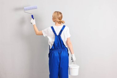 Kadın işçi duvarları boyuyor. Kapalı alanda patenli, arka manzaralı.