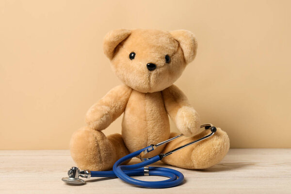 Pediatrics concept. Teddy bear with stethoscope on wooden table against beige background