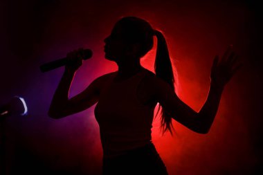 Karanlık arka planda şarkı söyleyen kadın silueti