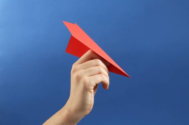 Mavi arka planda kırmızı kağıttan uçağı olan kadın, yakın plan.