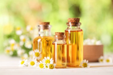 Beyaz ahşap masada, bulanık arka planda, yakın planda, gerekli yağ ve papatya çiçekleri.