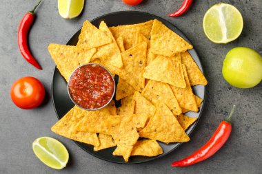 Nachos ile servis edilen lezzetli salsa sosu ve gri desenli masa üzerinde servis edilen ürünler.