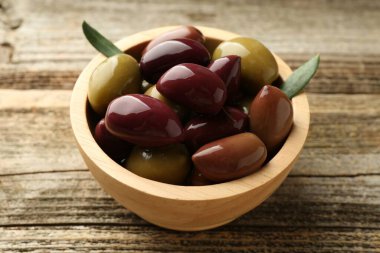 Lezzetli marine edilmiş zeytinler kasede ve ahşap masada yeşil yapraklar, yakın plan.