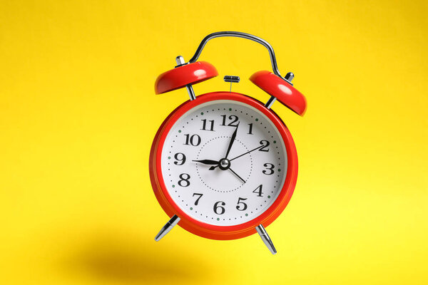 Красный будильник в воздухе на желтом фоне