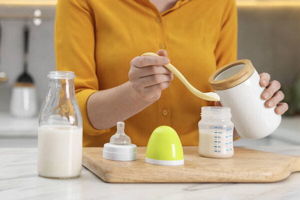 Mother making baby formula in feeding bottle at table indoors, closeup