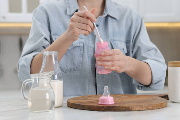 Mother making baby formula in feeding bottle at table indoors, closeup