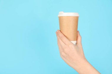 Açık mavi arka planda kağıt bardak tutan kadın, yakın plan. Tasarım için model