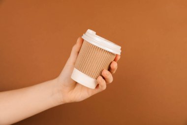 Kahverengi arka planda kağıt bardak tutan kadın, yakın plan. Tasarım için model