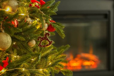 Evdeki şöminenin yanında at oyuncağı, diğer süsler ve festival ışıklarıyla süslenmiş güzel bir Noel ağacı, yakın çekim. Metin için boşluk