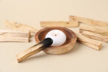 Palo Santo çubukları, yanmış bir tane ve bej arka planda yanan bir mum, yakın plan.