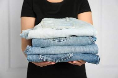 Kapalı alandaki aydınlık duvarın yanında farklı şık kot pantolonları olan kadın, yakın plan.