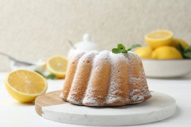 Beyaz ahşap masada pudra şekerli, nane ve narenciye meyveli lezzetli limonlu pasta, yakın plan.