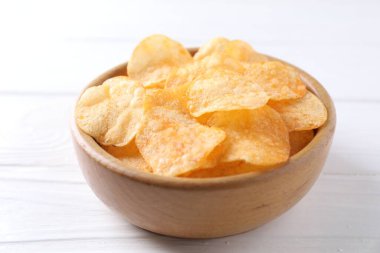Beyaz ahşap masada kasede patates cipsi, yakın plan.