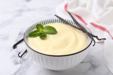 Lezzetli vanilyalı puding, nane ve kapsüller beyaz mermer masada, yakın plan.
