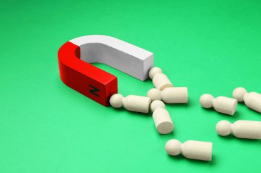 Yeşil arka planda insan figürlerini çeken mıknatıs, yakın plan