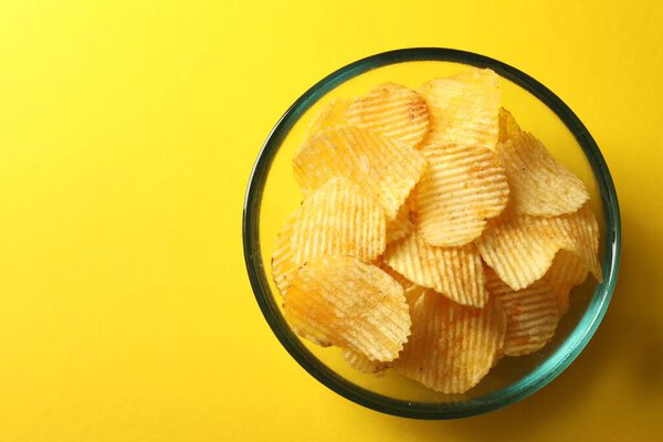 Вкусные картофельные чипсы на желтом фоне, вид сверху. Пространство для текста