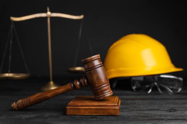 İş yerinde kaza oldu. Gavel, pullar ve inşaat işçilerinin koruyucu giysileri siyah ahşap masada, seçici odaklı.