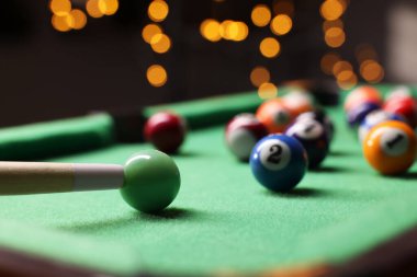 Many colorful billiard balls and cue on green table indoors, closeup