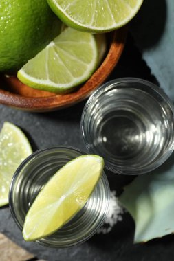 Limon dilimli tekila kadehleri, masada tuz ve agave yaprakları.