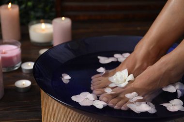Kadın ayaklarını su ve çiçeklerle kaseye daldırıyor, yakın plan. Spa tedavisi