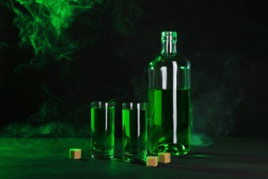 Absinthe shot bardakları, şişe ve esmer şeker siyah arka planda dumanlı