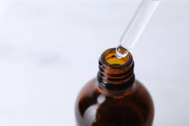 Işık arka planında pipetten şişeye serum damlatıyor, yakın plan. Metin için boşluk