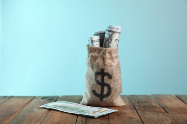 Çuval çuvalı ve üzerinde dolar banknotları açık mavi arka planda ahşap masa