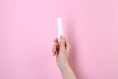 Pembe arka planda krem tübü olan kadın, yakın plan. Vücut bakımı ürünü