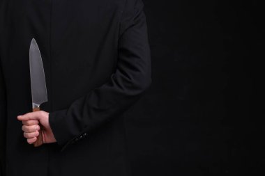 Siyah arka planda sırtında bıçak tutan bir iş adamı, yakın plan. Metin için boşluk