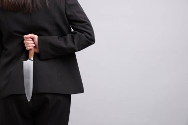 Arkasından bıçaklı iş kadını açık gri arka planda, yakın plan. Metin için boşluk