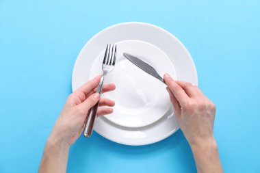 Açık mavi arka planda boş tabaklar üzerinde çatal bıçak takımı olan kadın.