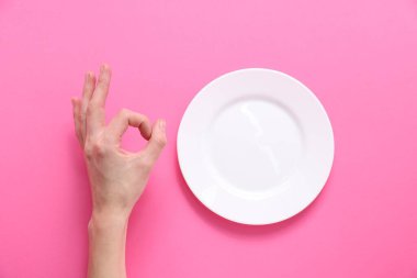 Pembe arka planda boş tabağın yanında iyi niyet gösteren bir kadın.
