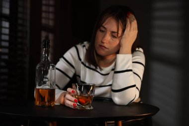 Alkol bağımlılığı. İçerideki masada elinde viski ve şişe olan bir kadın.