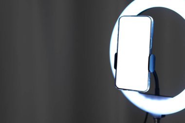 Gri perdenin yanında akıllı telefonu olan parlak bir lamba, yakın plan. Metin için boşluk