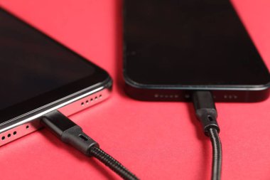 Kırmızı arkaplanda akıllı telefonlara bağlı USB şarj kabloları, yakın plan