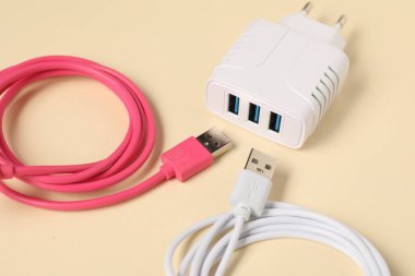 USB güç adaptörü ve bej arkaplandaki şarj kabloları, yakın plan