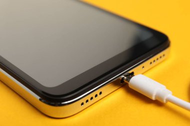USB şarj kablosu turuncu arka plandaki akıllı telefona bağlı, yakın plan