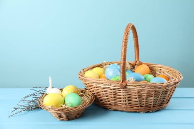 Birçok süslü Paskalya yumurtası hasır sepetlerde ve söğüt dallarında açık mavi ahşap masada