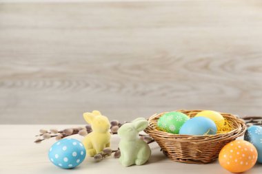 Hasır sepette birçok süslü Paskalya yumurtası, söğüt dalları ve ahşap masada dekoratif tavşanlar, metin için yer.