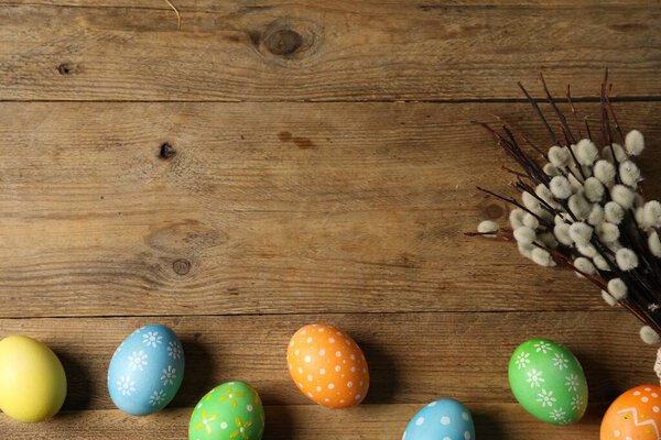 Beautiful decorated Easter eggs and willow branches on wooden table, flat lay. Space for text