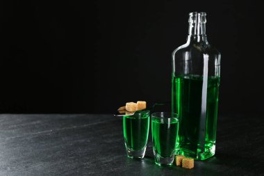 Absinthe shot bardaklarında, şişede, esmer şekerde ve siyah arkaplanda siyah kaşıkta, mesaj için boşluk