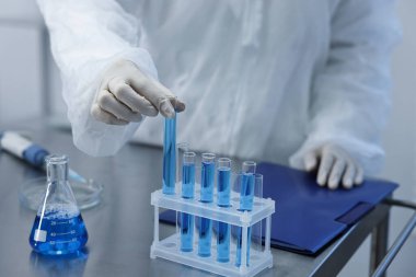 Bilim adamı laboratuarda mavi numuneyle test tüpü alıyor, yakın plan.