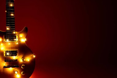 Koyu kırmızı arka planda Noel ışıkları olan elektro gitar, yakın plan. Metin için boşluk