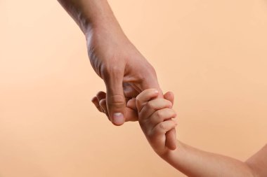 Baba ve çocuk bej arka planda el ele tutuşuyorlar, yakın plan.