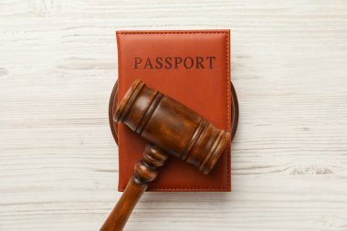 Kahverengi kapaklı pasaport ve beyaz masa üzerinde yargıç tokmağı.