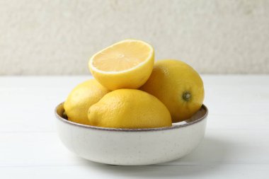 Taze taze ve limonları kaseye koyup beyaz ahşap masaya koyun. Yakın plan.