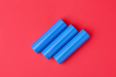 Kırmızı arkaplanda üç AA cep telefonu pili, üst görünüm