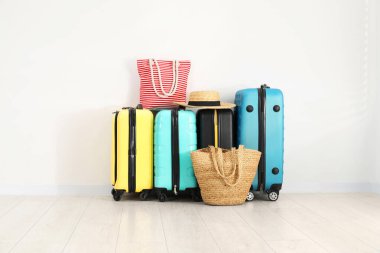 Renkli bavullar, plaj çantaları ve beyaz duvarın yanında hasır şapka.