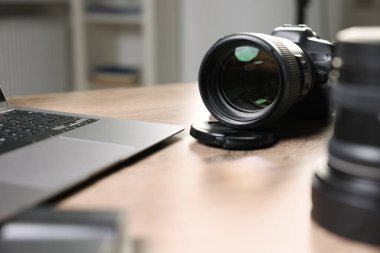 Profesyonel fotoğraf makinesi, lens ve laptop ahşap masada, seçici odak