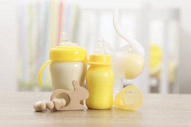 İçerideki ahşap masada süt, göğüs pompası ve oyuncakla beslenen şişeler.